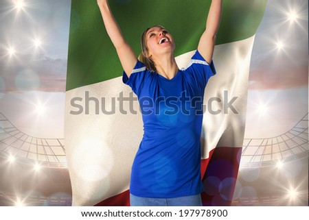 Cheering football fan in blue jersey holding italy flag against large football stadium under cloudy blue sky