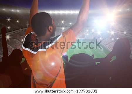 Cheering football fan in orange jersey against large football stadium with lights
