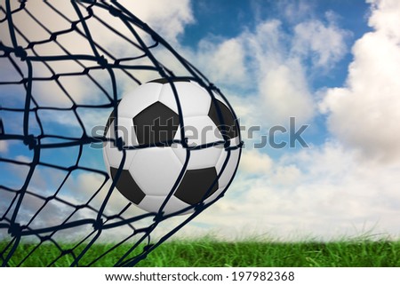 Composite image of football in back of the net against green grass under blue sky
