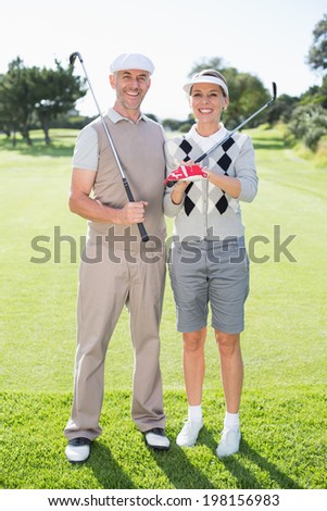 Golfing couple smiling at camera holding clubs on a sunny day at the golf course