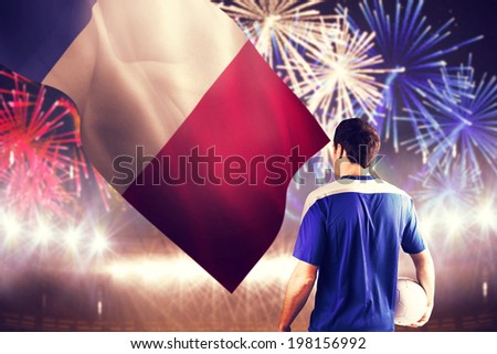 Handsome french football player holding the ball against fireworks exploding over football stadium