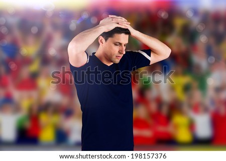 Disappointed football player looking down against blurry football pitch with crowd