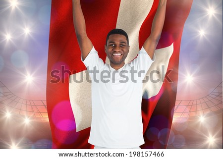 Excited handsome football fan cheering holding swiss flag against large football stadium under purple sky