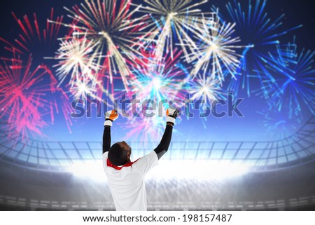 Excited goalkeeper in white cheering against fireworks exploding over football stadium