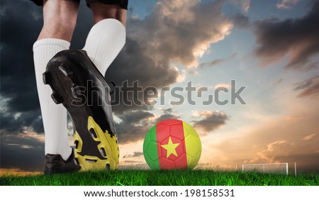 Composite image of football boot kicking cameroon ball against green grass under blue and orange sky