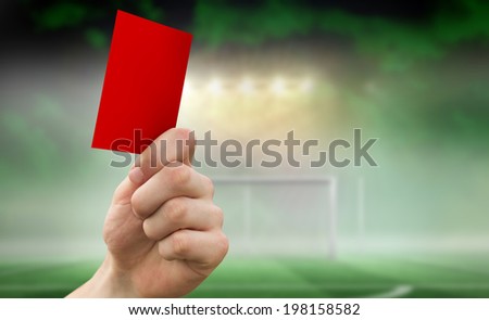 Hand holding up red card against football pitch under spotlights