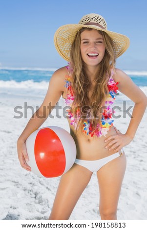 Fit smiling blonde in white bikini and straw hat holding beach ball on a sunny day