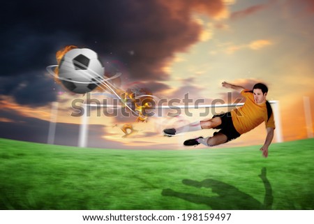 Football player in orange kicking against football pitch under cloudy orange sky