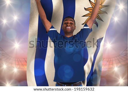 Cheering football fan in blue jersey holding uruguay flag against large football stadium under purple sky