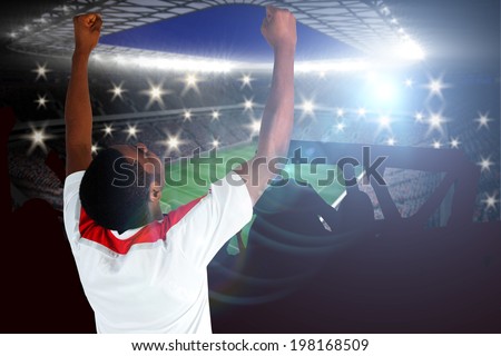 Excited handsome football fan cheering against large football stadium with lights