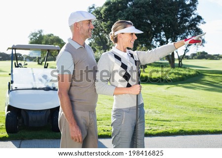 Happy golfing couple looking at course with golf buggy behind on a sunny day at the golf course