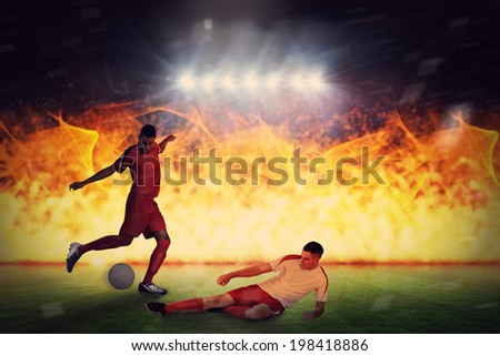 Football players tackling for the ball against football pitch under spotlights