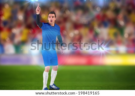 Football player raising his hand against blurry football pitch with crowd