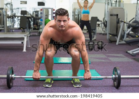 Shirtless bodybuilder about to lift heavy barbell at the gym