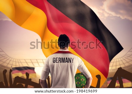 Germany football player holding ball against large football stadium under bright blue sky
