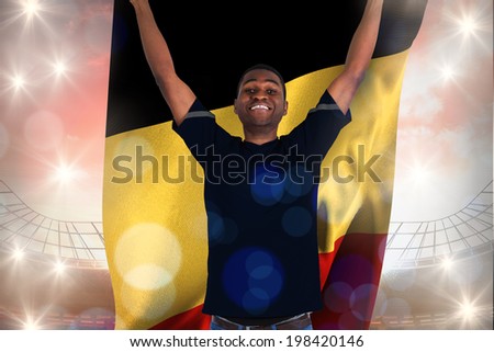 Excited football fan in black cheering holding belgium flag against large football stadium under cloudy blue sky