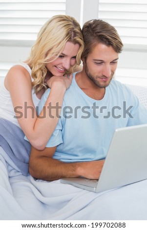 Happy casual couple sitting on couch using laptop at home in the living room
