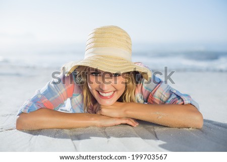 Pretty blonde smiling at camera at the beach lying on the sand on a sunny day