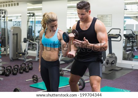Personal trainer coaching female bodybuilder lifting dumbbell at the gym