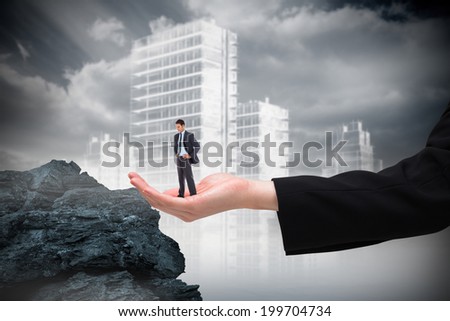 Serious businessman with hands on hips in large hand against large rock overlooking outline of city