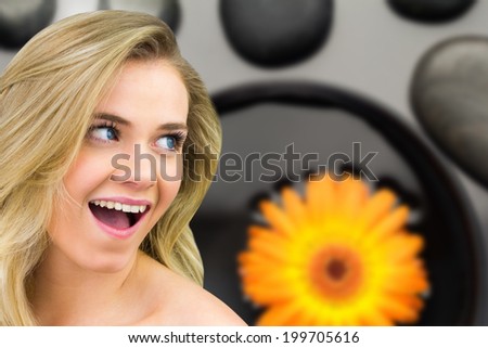Smiling blonde natural beauty against orange flower floating in bowl with pebbles