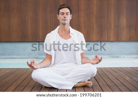 Handsome man in white meditating in lotus pose in health spa