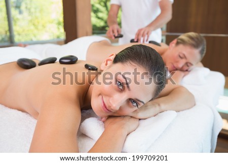 Pretty friends lying on massage tables with hot stones on their backs in the health spa