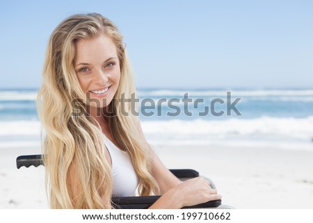 Wheelchair bound blonde smiling at the camera on the beach on a sunny day