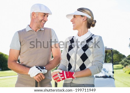 Happy golfing couple facing each other with golf buggy behind on a sunny day at the golf course