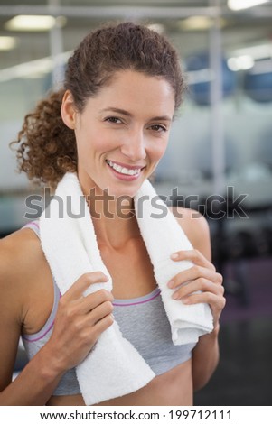 Fit woman smiling at camera with towel around shoulders at the gym