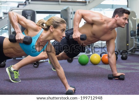 Bodybuilding man and woman holding dumbbells in plank position at the gym