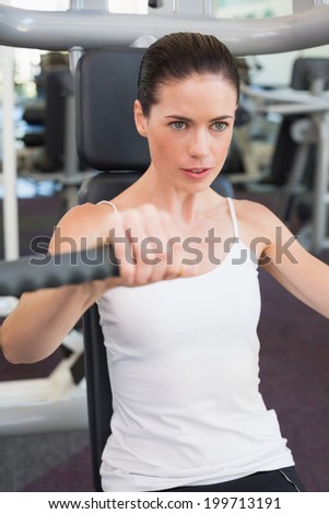 Fit brunette using weights machine for arms at the gym