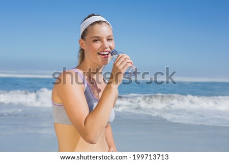 Sporty happy blonde drinking water on the beach on a sunny day