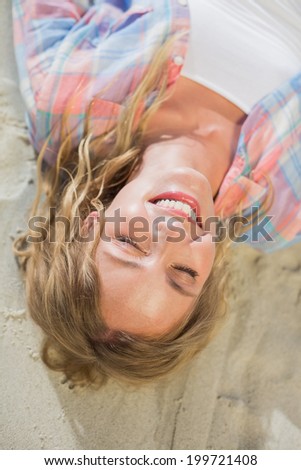 Pretty blonde smiling at the beach lying on the sand on a sunny day