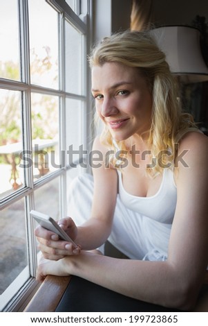 Pretty blonde sitting by the window sending a text at home in the living room