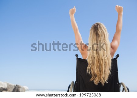 Wheelchair bound blonde sitting on the beach with arms up on a sunny day