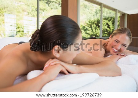 Happy friends lying on massage tables with hot stones on their backs in the health spa