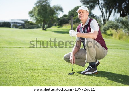 Confident golfer kneeling holding his golf club on a sunny day at the golf course