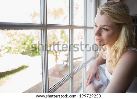 Pretty blonde looking out the window at home in the living room
