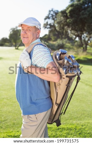 Golfer standing holding his golf bag smiling at camera on a sunny day at the golf course