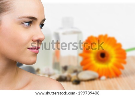 Smiling blonde natural beauty against beauty products with flower and pebbles