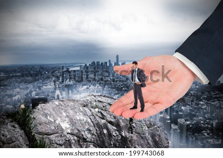 Serious businessman with hands on hips in large hand against large rock overlooking huge city