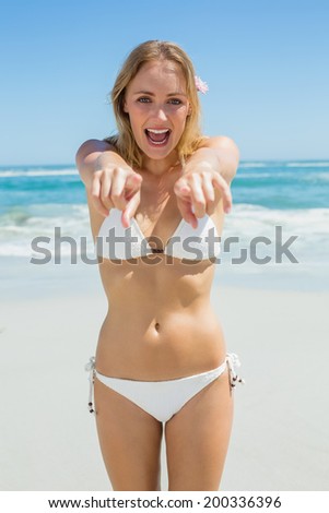 Beautiful blonde smiling and pointing at camera on the beach on a sunny day