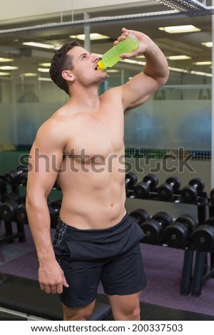 Shirtless bodybuilder drinking sports drink at the gym