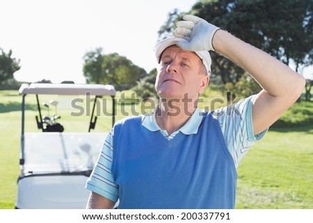 Happy golfer looking at camera with golf buggy behind on a sunny day at the golf course