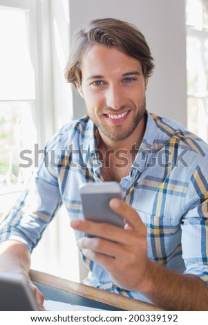 Smiling casual man using laptop and texting on smartphone at home in the living room