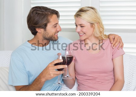 Happy couple drinking red wine together on the couch at home in the living room