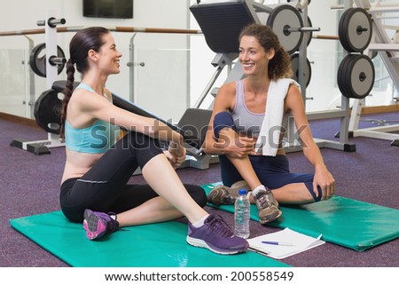 Fit friends chatting together on exercise mats at the gym