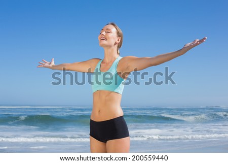 Fit woman standing on the beach with arms out on a sunny day