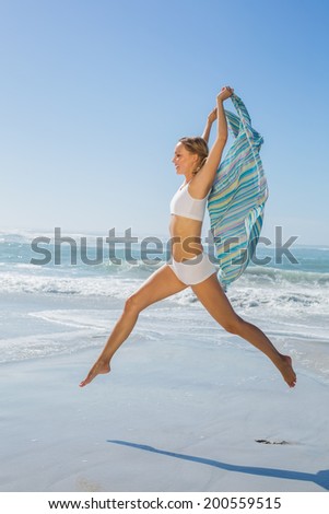 Gorgeous fit blonde leaping by the sea with scarf on a sunny day